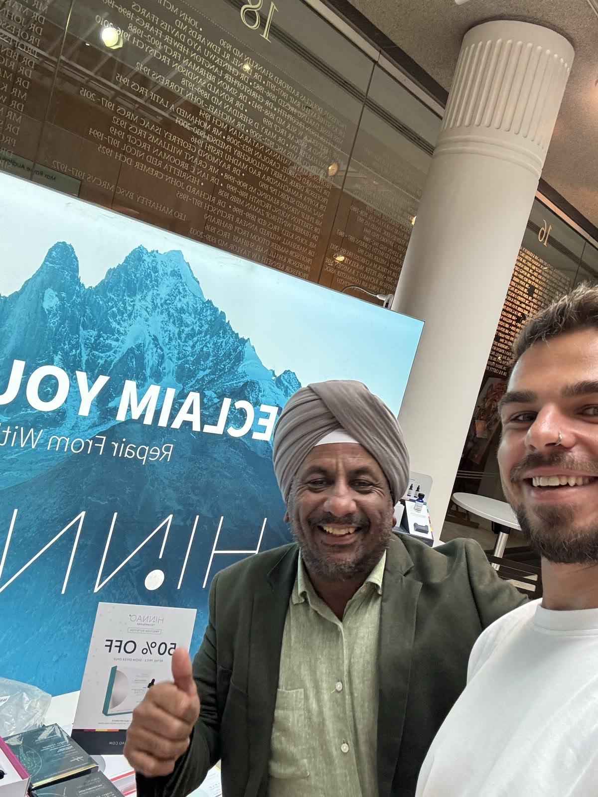 Two attendees smiling together beside the HINNAO display at the Royal Society of Medicine